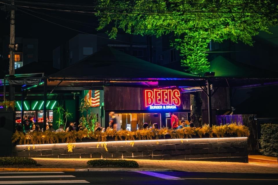 Fachada do Beeis Burger e Brasa à noite, com clientes nas mesas, em Ivoti